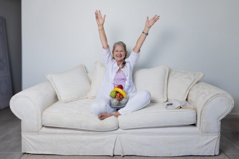 Wellness branding photo of practitioner with arms excitedly outstretched and bowl of fruit in lap