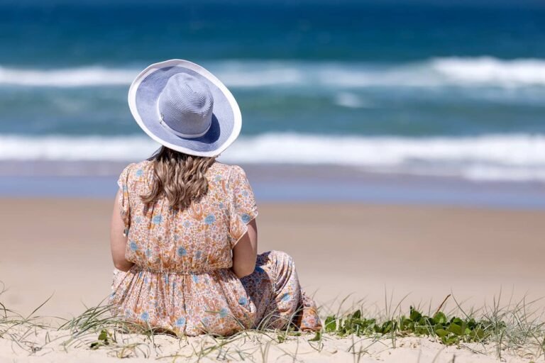 Lifestyle branding photo for wellness practitioner sitting on top of dune looking out to the ocean wearing sunhat for wellness and personal branding photo