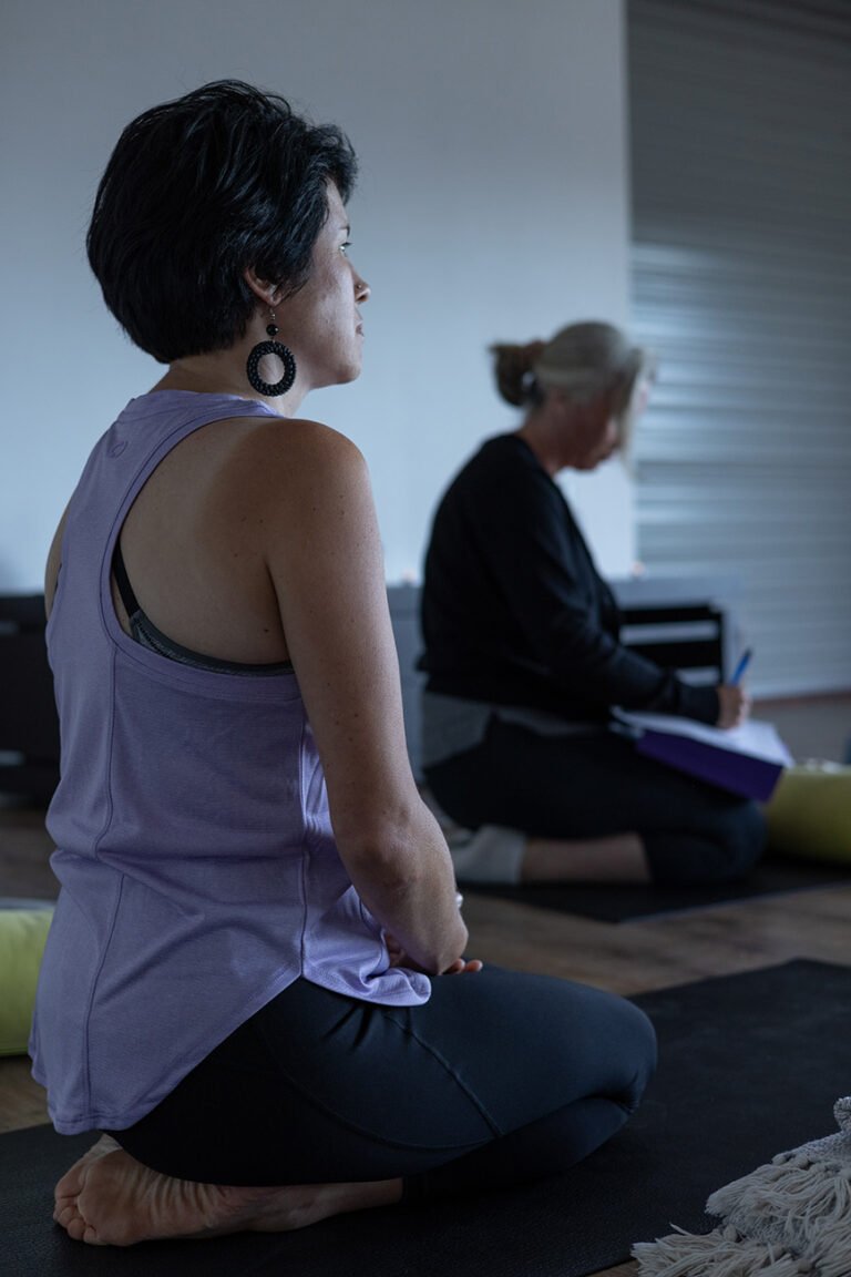 Women participating in yoga session with main woman sitting on feet and gazing in front of her for wellness branding photo