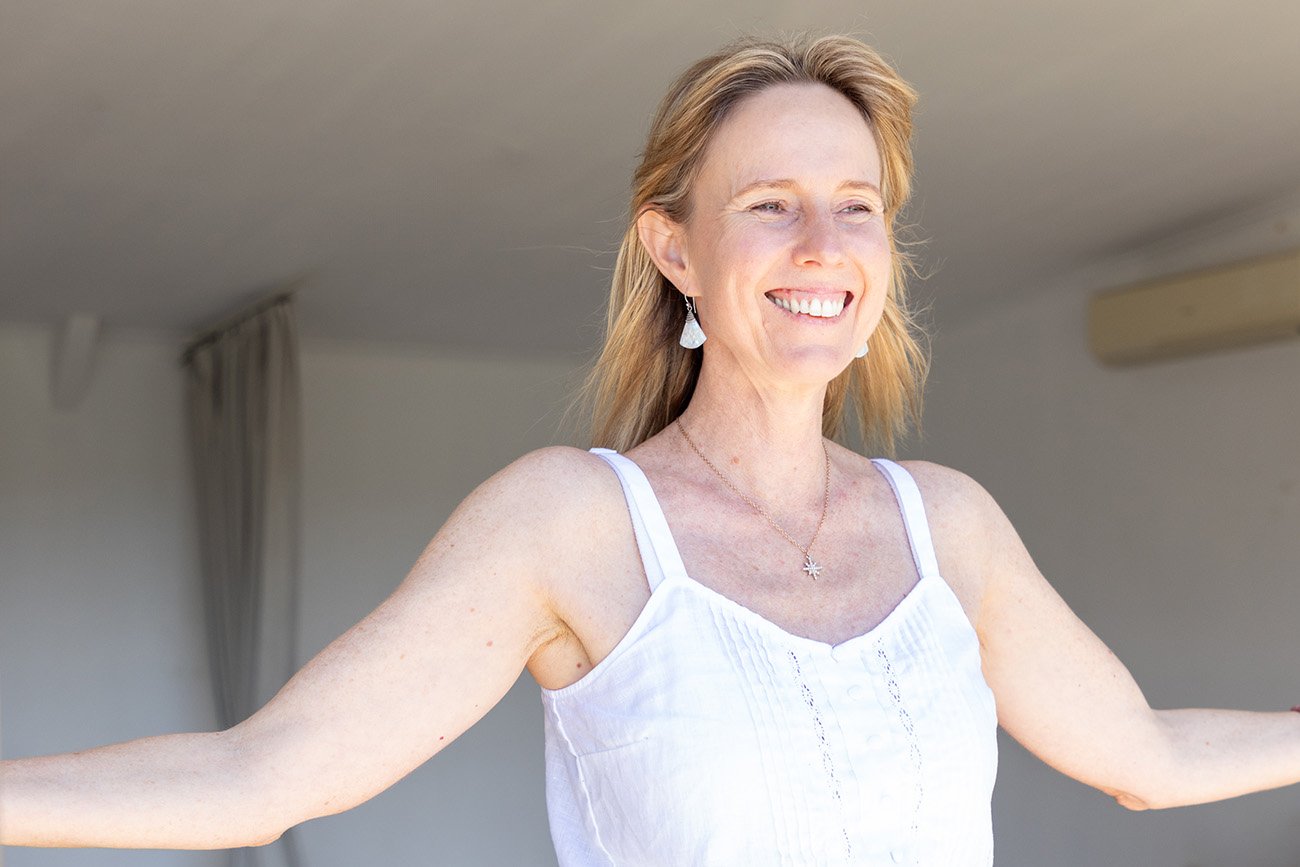 Female naturopath embodying session at women's retreat with arms outstretched and smiling